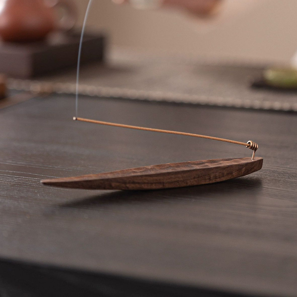 Black walnut incense holder with incense stick burning, side angle on dark wood table