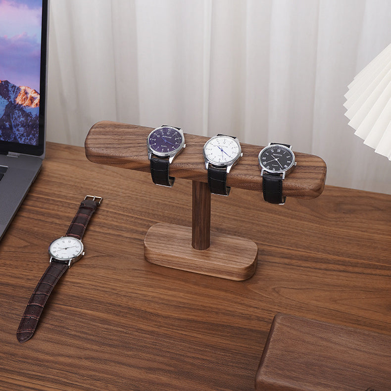 Handcrafted black walnut watch stand displaying three wristwatches with natural wood grain on a desktop.