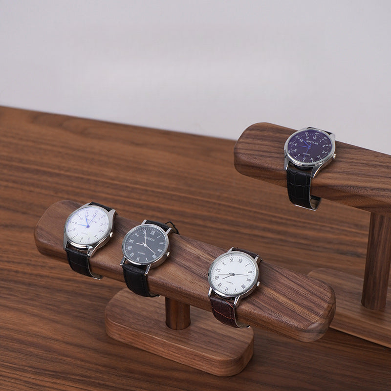 Black walnut wooden watch stand organizing three wristwatches on a clean desktop.
