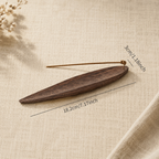 Side view of a handcrafted black walnut incense holder with a lit incense stick on a wooden table.