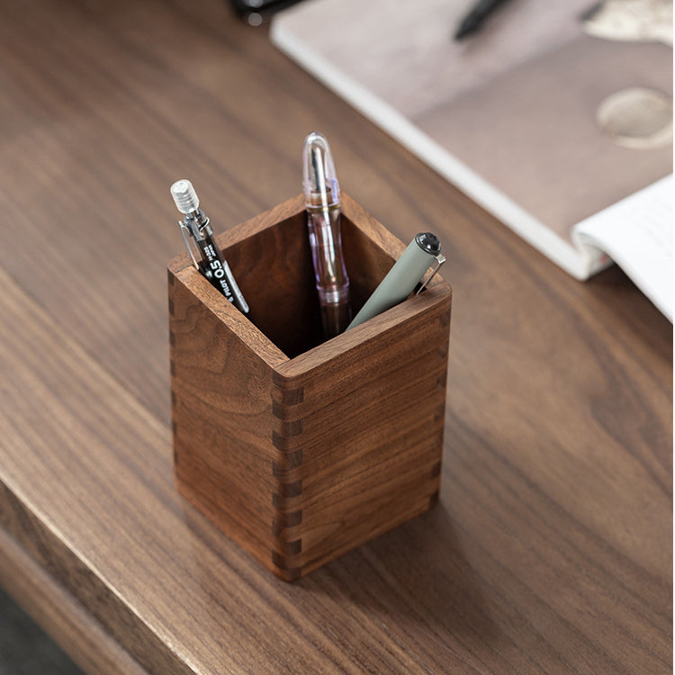 Black walnut wooden pen holder neatly organizing writing tools on an office desk.
