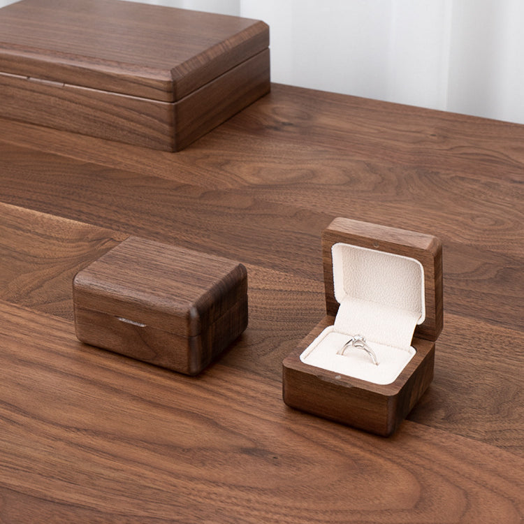Personalized black walnut ring box styled on a wooden table beside jewelry for engagement and wedding moments.
