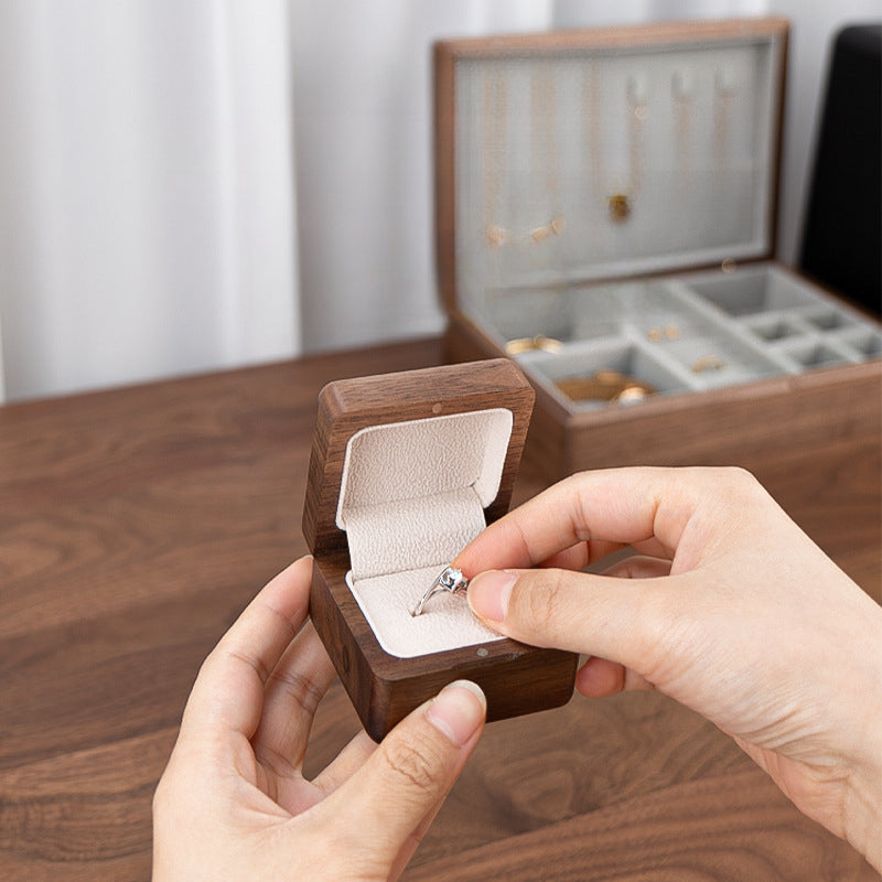 Handcrafted personalized black walnut ring box holding an engagement ring with soft velvet lining.