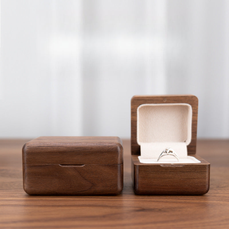 Open black walnut ring box displaying a diamond engagement ring with soft interior lining.