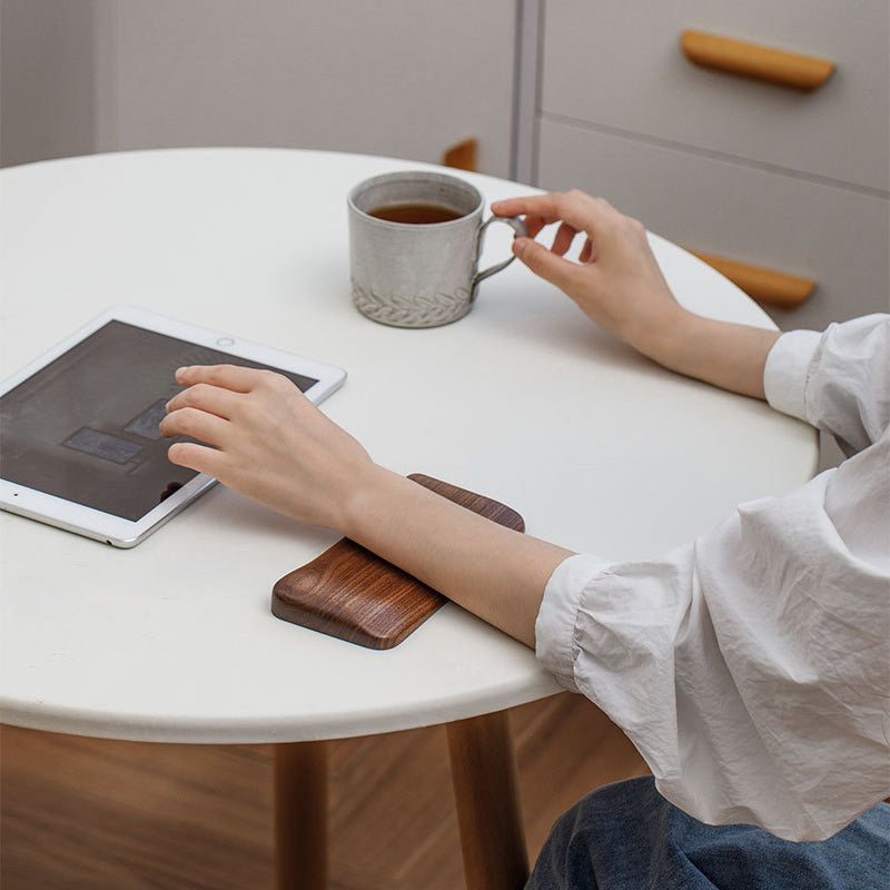 Solid black walnut wood mouse wrist rest placed beside a mouse and keyboard on a modern workspace.