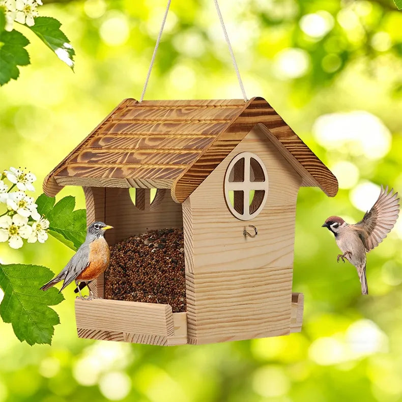 Wooden hanging bird feeder suspended from a tree branch in a backyard garden.