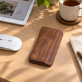 Black walnut mouse wrist rest with a smooth curved shape, displayed on a desk in warm natural light.