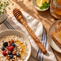 Olive wood honey dipper with natural grain, styled beside honey and breakfast foods in warm natural light.